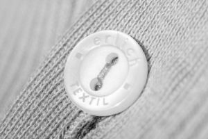 Der Knopf an einem Kleidungsstück von Erlich Textil mit Schriftzug